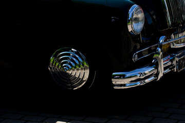 close-up of vintage classic car chrome details and round grille reflecting pavement and green trees...