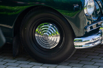 vintage classic car wheel close-up with chrome hubcap and black tire reflecting trees on sunny day...