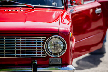 red vintage soviet car front headlight and chrome grille detail with open door on sunny day at...
