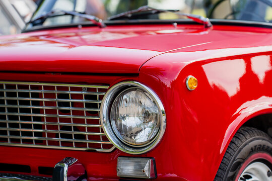 close up of red vintage classic car front with chrome headlight and grill retro vehicle from automobile exhibition showcasing antique design oldtimer transportation icon from 1970s sunny outdoor show - Powered by Adobe