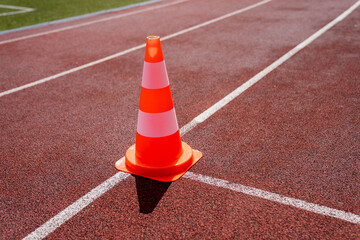 orange traffic cone on red athletic running track in bright sunlight safety symbol on stadium...