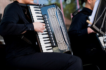 Musician playing accordion during live outdoor concert. Hands and black accordion in performance...