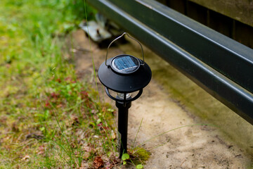 black solar garden path light on grass and soil near metal fence, eco friendly outdoor lighting...