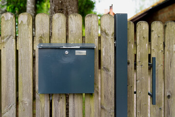 modern black metal mailbox on wooden fence gate outside suburban home, secure post box design for...
