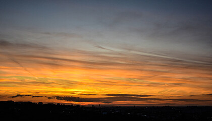 Warm sunset sky over city with illuminated clouds and colors