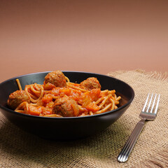 Spaghetti al sugo con polpette nel piatto nero, spazio per testo