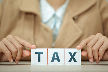 Person’s hand showing three wooden blocks spelling out the word TAX