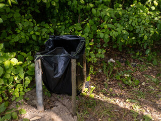 A black trash can sitting in the middle of a forest