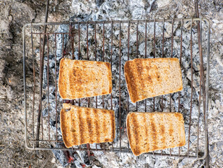 Four slices of bread are cooking on a grill over a campfire