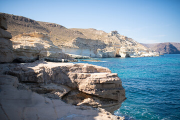 Rocky coastline with clear turquoise waters and rugged cliffs under a bright blue sky, showcasing...