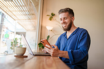 A Smiling Young Man is Clearly Focused on His Laptop While Working in a Cozy Cafe Environment