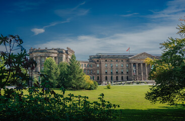 Fototapeta premium Elegant frontal view of Schloss Wilhelmshöhe, Kassel with its classical colonnade and flag-topped roof, surrounded by a green park landscape.