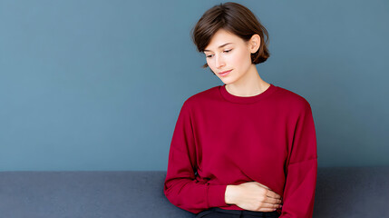 Young woman sits on sofa experiencing stomach ache. Holds belly. Painful menstrual cramps. Home setting. Indoor shot. Female suffering. Possible period discomfort. Possible digestive issues. Woman