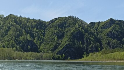 Discover a peaceful river flowing through a lush green forest, framed by a stunning rocky cliff. Ideal for tourism and inspiration, this scene captures the beauty of nature.