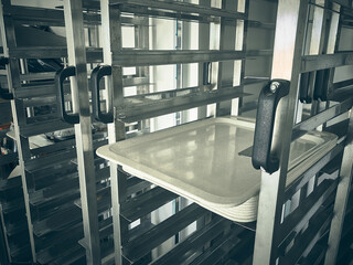 Beige food trays placed in a multi-level metal rack. Stacked food trays in industrial kitchen rack