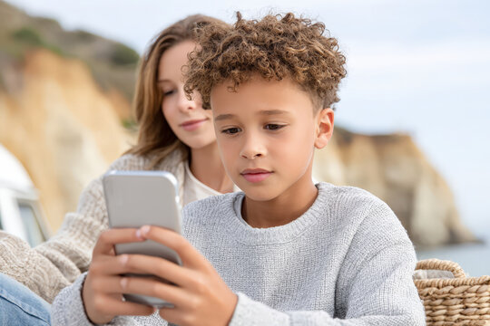 Young multiracial boy with phone and caucasian woman in outdoor setting