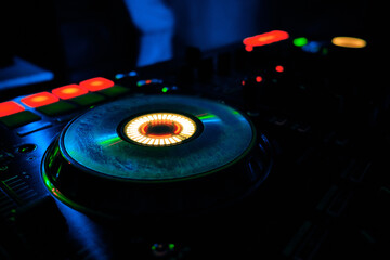 Professional DJ mixer illuminated by colorful LED lights in a dark environment. Nightclub atmosphere. Music equipment, electronic sound control