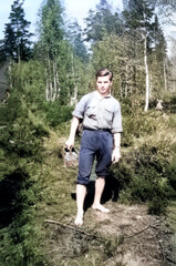 Vintage portrait of a young guy walking barefoot in the forest holding sneakers in his hands. Retro...