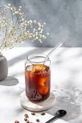 Cold brew coffee in a glass with ice on a light background with coffee beans