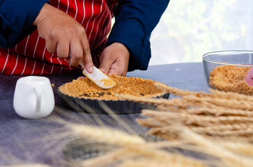 Baker wearing red and white striped apron spreading golden graham cracker crumbs into fluted tart...
