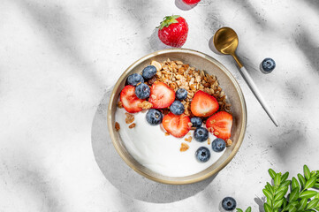 Natural greek yogurt with granola, blueberry and strawberry in a bowl on a light background