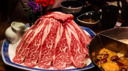 close up of slices of raw uncooked marbled beef in a hill for hot pot. The spicy hot pot on the side
