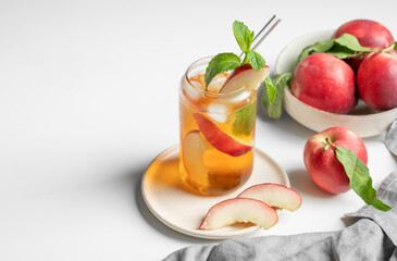 Ice tea with peach, mint in a glass on a white table near window with fresh fruits, napkin and sunlight.