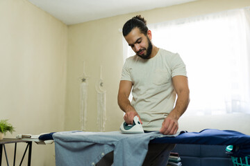 Man with a beard ironing clothes on ironing board at home