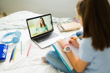 Little girl taking notes while learning online with her teacher