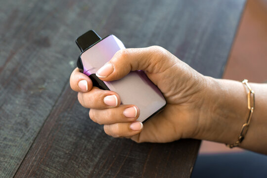 Close-up of female hand holding modern purple vape device on wooden table, concept of smoking alternatives, theme of lifestyle, habits, technology