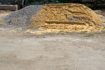 A large mound of gravel and sand is seen at a construction site, with a worker positioned nearby,...
