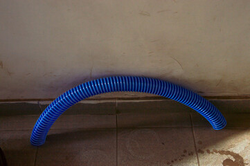 A curved blue pipe lies against a wall on the floor of a room with tiled flooring, creating an...