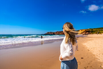 Portrait of beautiful mature woman walking on sandy beach on summer windy day. Side view. Amado beach on Algarve coast in Portugal	