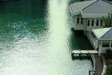 Architectural photograph of a modern white villa built over a calm green lake, with a wooden pier...
