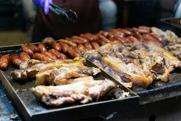 Juicy slices of grilled wild boar meat being roasted over open flames at a night market food stall. The smoky aroma and charred edges highlight the rustic and flavorful appeal of traditional street cu