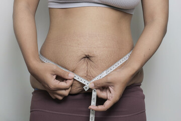 woman measure her postpartum belly with stretch marks, problem after giving birth. promoting body positivity and the reality of motherhood