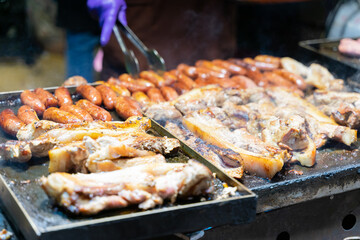 Juicy slices of grilled wild boar meat being roasted over open flames at a night market food stall. The smoky aroma and charred edges highlight the rustic and flavorful appeal of traditional street cu