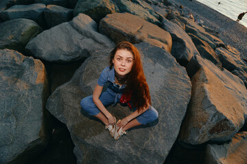 lifestyle woman in modern boho-western denim street style sitting on rocks at sunset, film color...