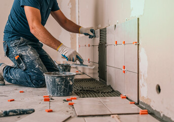 Construction worker laying ceramic tiles on a wall using adhesive and spacers during renovation
