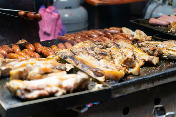 Juicy slices of grilled wild boar meat being roasted over open flames at a night market food stall. The smoky aroma and charred edges highlight the rustic and flavorful appeal of traditional street cu