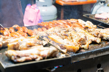 Juicy slices of grilled wild boar meat being roasted over open flames at a night market food stall. The smoky aroma and charred edges highlight the rustic and flavorful appeal of traditional street cu