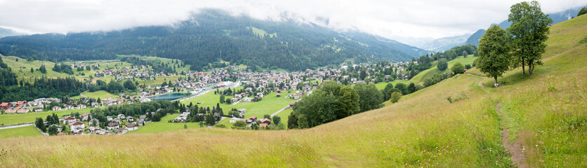 panoramic view to tourist resort Klosters, hiking path through green pasture, swiss destination