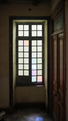 Old multi-pane window with frosted and slightly tinted glass panels set in a worn, dark wooden frame. Old wooden window with frosted glass in dim hallway