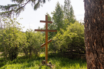 A wooden Orthodox cross stands peacefully in a lush green field under a bright, sunny sky....