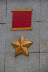 A close-up of a golden star and red rectangle on a stone wall. Gold Star Medal of the Hero of the...