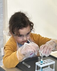 Little cute girl wearing safety goggles conducts chemical experiments with liquid in test tubes.