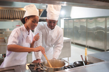 African American Female and Black male chefs in white uniforms and hats stirring pot together,...