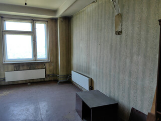 An interior shot of an abandoned, neglected room with peeling wallpaper and a cabinet.