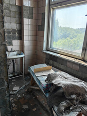 A decaying medical room with a window overlooking a lush, green landscape.