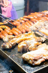 Juicy slices of grilled wild boar meat being roasted over open flames at a night market food stall. The smoky aroma and charred edges highlight the rustic and flavorful appeal of traditional street cu
